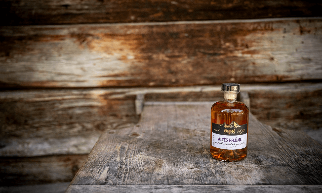 Altes Pflümli auf einem Holztisch. Im Hintergrund ist eine Holzhütte.